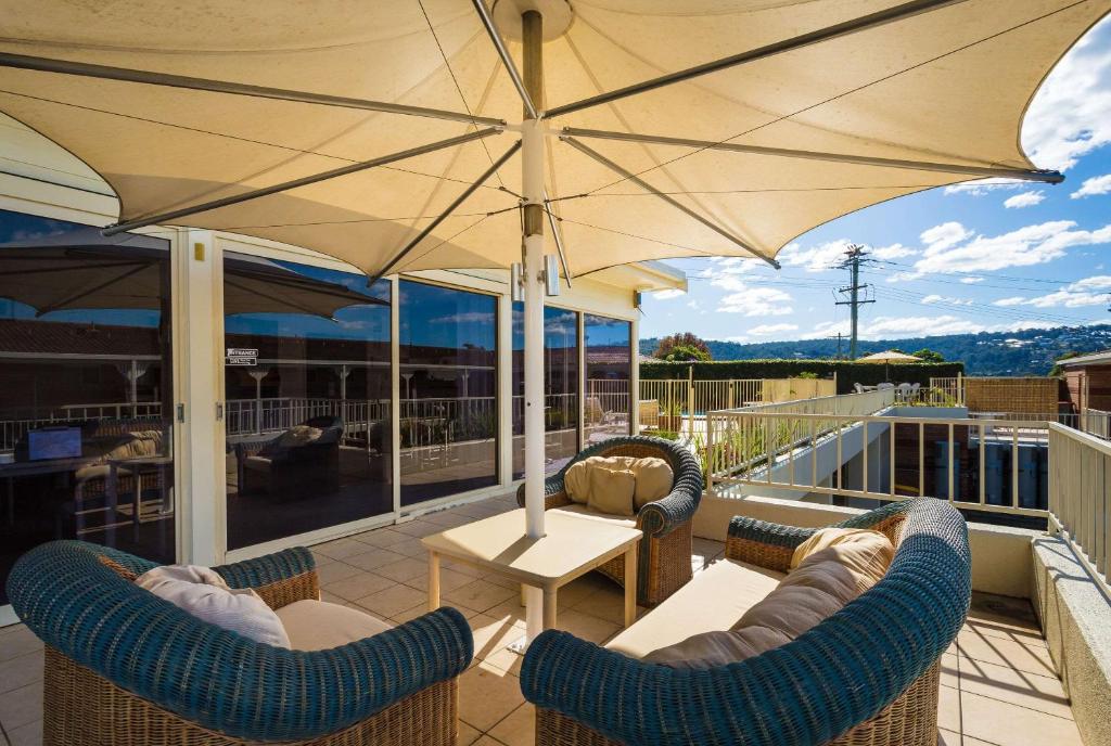 Sunny outdoor terrace with shade umbrella and lounge seating overlooking the pool and Merimbula hills
